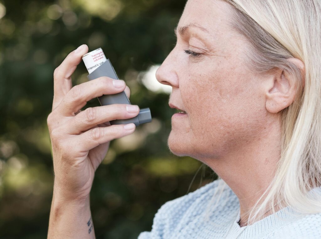 Woman using an inhaler outdoors to manage her respiratory condition effectively.